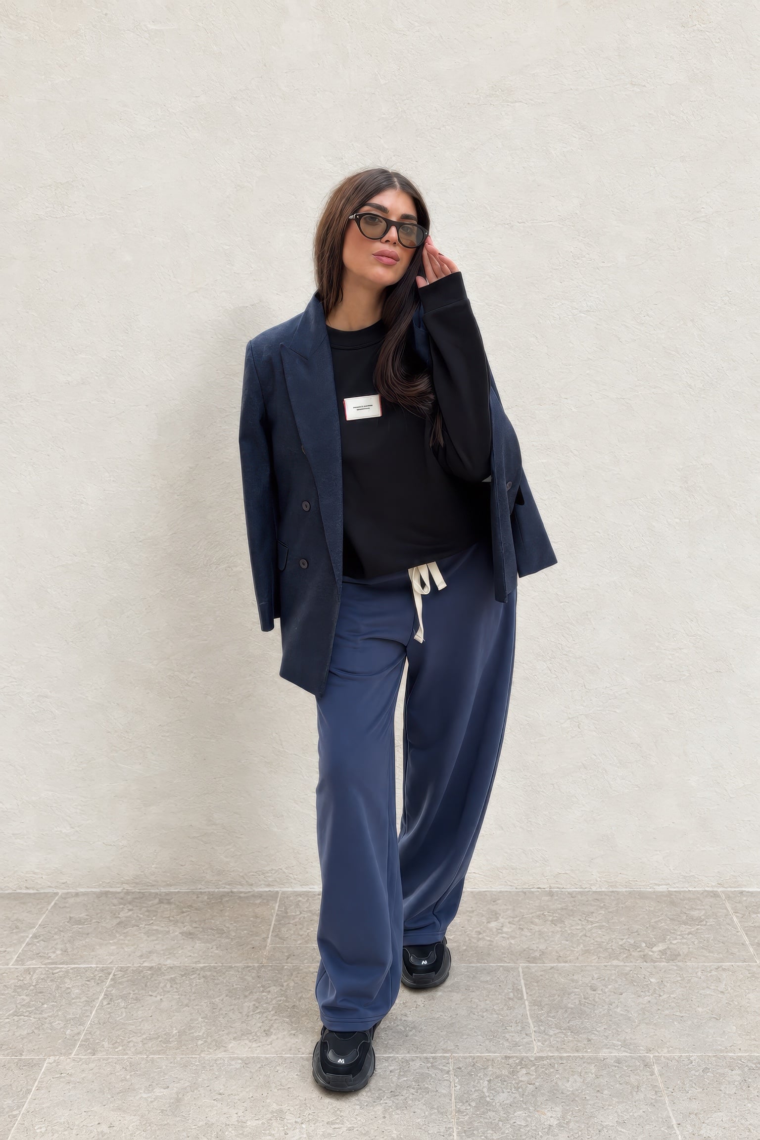 Omuza alınmış lacivert blazer ceket, siyah sweatshirt ve lacivert bağcıklı geniş paça pantolonla bir kombin